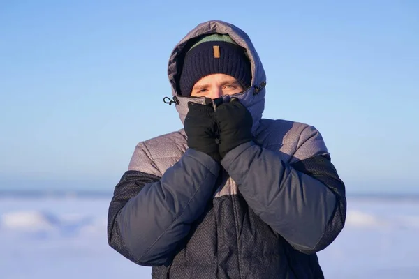 Portrait of frozen guy, handsome freezing man standing walking outdoors at north at winter snowy cold frosty day, shaking, trembling, shivering because of extreme low temperature in jacket, hat, hood — стоковое фото