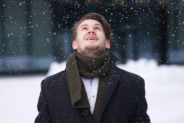 Portrait of happy positive excited guy, young cheerful handsome man in formal clothes, businessman is having fun, enjoying falling snow, cold winter snowy day looking up the sky catches snowflakes — Stock fotografie