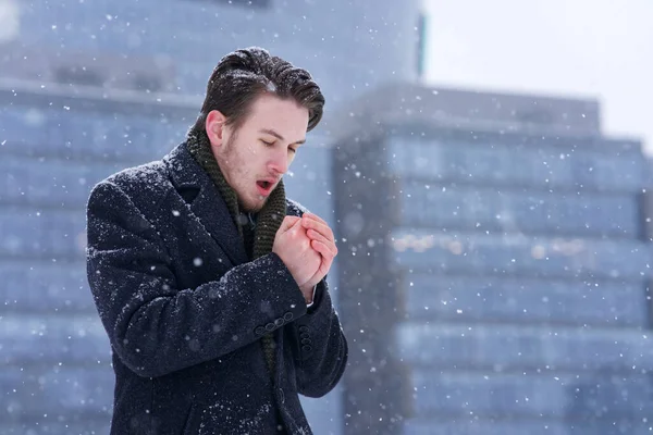 Portrait of frozen handsome guy in formal coat, young handsome freezing man standing walking outdoors at winter snowy cold frosty day, shaking, trembling, shivering, warming, trying to warm his hands