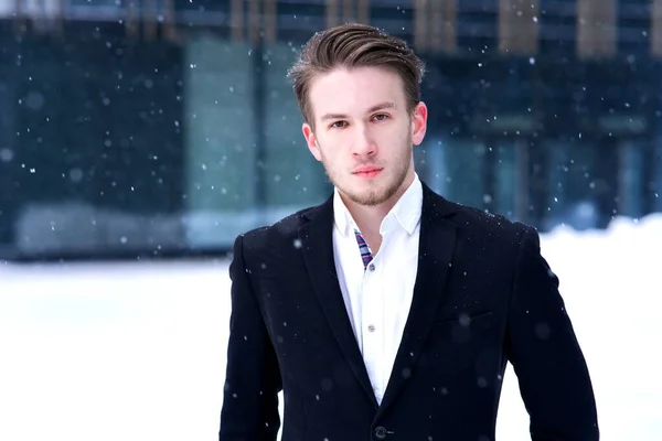 Portrait of handsome serious frozen guy, young blonde European man office worker in formal clothes, suit jacket and white shirt standing outdoors looking at camera at winter cold snowy day in snow — Stock fotografie