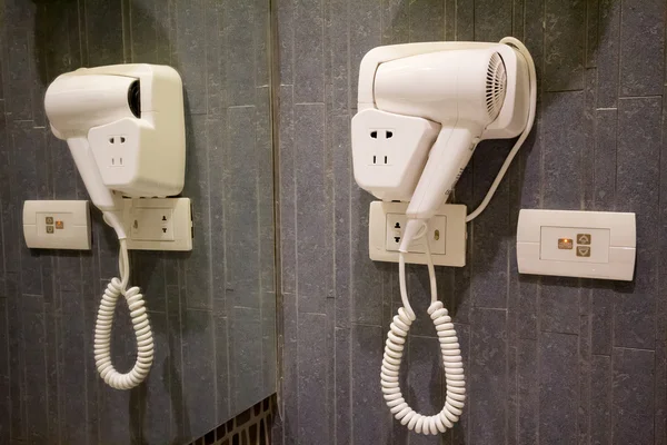Banyoda duvarda beyaz saç kurutma makinesi var.