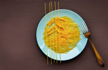 Kahverengi masa örtüsü üzerinde turkuaz bir tabak çiğ makarna.