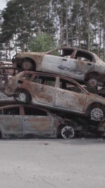 Bu stok dikey video Irpin, Bucha bölgesinde gri, düz, renksiz, yanmış arabaları gösteriyor.