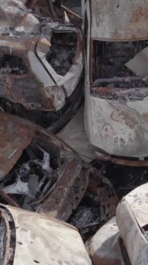 Bu stok dikey video Irpin, Bucha bölgesinde gri, düz, renksiz, yanmış arabaları gösteriyor.