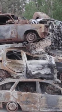 Bu stok dikey video Irpin, Bucha bölgesinde gri, düz, renksiz, yanmış arabaları gösteriyor.