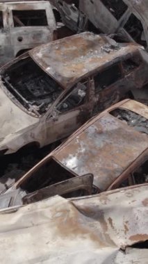 Bu stok dikey video Irpin, Bucha bölgesinde gri, düz, renksiz, yanmış arabaları gösteriyor.