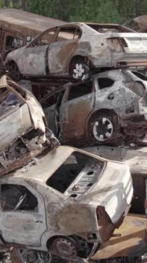 Bu stok dikey video Irpin, Bucha bölgesinde gri, düz, renksiz, yanmış arabaları gösteriyor.