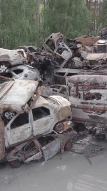 Bu stok dikey video Irpin, Bucha bölgesinde gri, düz, renksiz, yanmış arabaları gösteriyor.