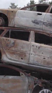 Bu stok dikey video Irpin, Bucha bölgesinde gri, düz, renksiz, yanmış arabaları gösteriyor.