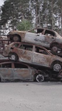 Bu stok dikey video Irpin, Bucha bölgesinde gri, düz, renksiz, yanmış arabaları gösteriyor.