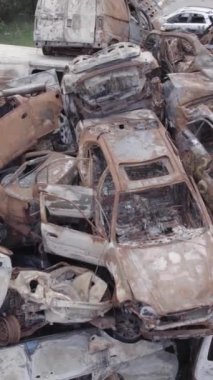 Bu stok dikey video Irpin, Bucha bölgesinde gri, düz, renksiz, yanmış arabaları gösteriyor.