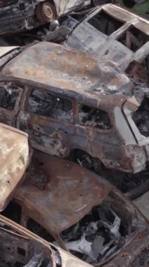 Bu stok dikey video Irpin, Bucha bölgesinde gri, düz, renksiz, yanmış arabaları gösteriyor.