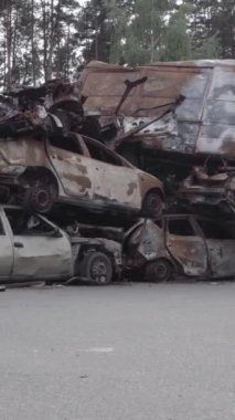 Bu stok dikey video Irpin, Bucha bölgesinde gri, düz, renksiz, yanmış arabaları gösteriyor.