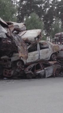Bu stok dikey video Irpin, Bucha bölgesinde gri, düz, renksiz, yanmış arabaları gösteriyor.