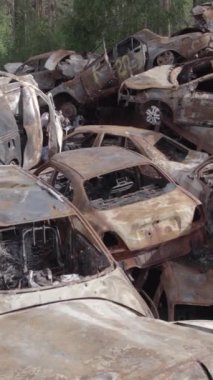 Bu stok dikey video Irpin, Bucha bölgesinde gri, düz, renksiz, yanmış arabaları gösteriyor.