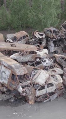 Bu stok dikey video Irpin, Bucha bölgesinde gri, düz, renksiz, yanmış arabaları gösteriyor.