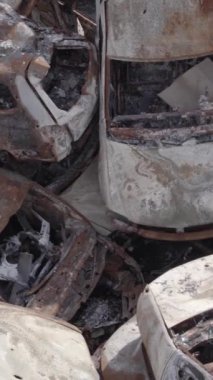 Bu stok dikey video Irpin, Bucha bölgesinde gri, düz, renksiz, yanmış arabaları gösteriyor.