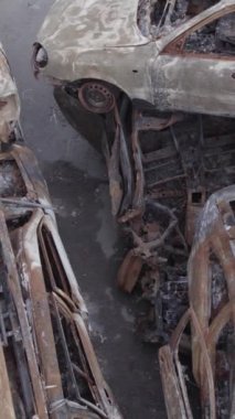 Bu stok dikey video Irpin, Bucha bölgesinde gri, düz, renksiz, yanmış arabaları gösteriyor.