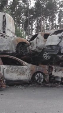 Bu stok dikey video Irpin, Bucha bölgesinde gri, düz, renksiz, yanmış arabaları gösteriyor.