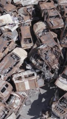 Bu stok dikey video Irpin, Bucha bölgesinde gri, düz, renksiz, yanmış arabaları gösteriyor.