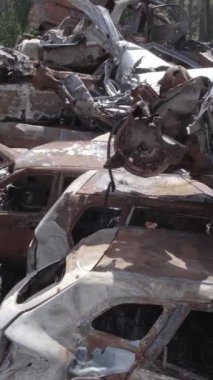 Bu stok dikey video Irpin, Bucha bölgesinde gri, düz, renksiz, yanmış arabaları gösteriyor.