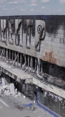 Bu stok dikey video, Bucha 'daki bir alışveriş merkezinin yıkık dökük bir binasını gösteriyor. Ağır çekim, gri, renksiz, düz.