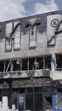 Bu stok dikey video, Bucha 'daki bir alışveriş merkezinin yıkık dökük bir binasını gösteriyor. Ağır çekim, gri, renksiz, düz.