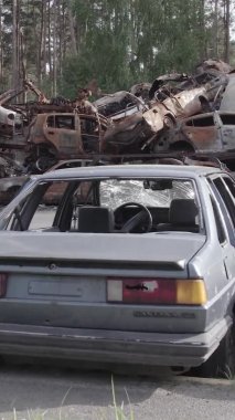 Bu stok dikey video Irpin, Bucha bölgesinde gri, düz, renksiz, yanmış arabaları gösteriyor.