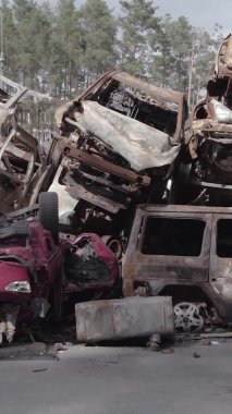 Bu stok dikey video Irpin, Bucha bölgesinde gri, düz, renksiz, yanmış arabaları gösteriyor.