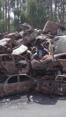 Bu stok dikey video Irpin, Bucha bölgesinde gri, düz, renksiz, yanmış arabaları gösteriyor.