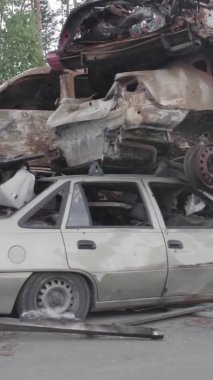 Bu stok dikey video Irpin, Bucha bölgesinde gri, düz, renksiz, yanmış arabaları gösteriyor.