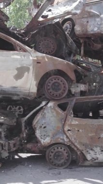 Bu stok dikey video Irpin, Bucha bölgesinde gri, düz, renksiz, yanmış arabaları gösteriyor.