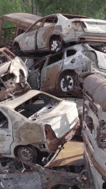 Bu stok dikey video Irpin, Bucha bölgesinde gri, düz, renksiz, yanmış arabaları gösteriyor.