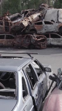 Bu stok dikey video Irpin, Bucha bölgesinde gri, düz, renksiz, yanmış arabaları gösteriyor.