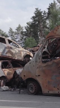 Bu stok dikey video Irpin, Bucha bölgesinde gri, düz, renksiz, yanmış arabaları gösteriyor.