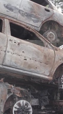 Bu stok dikey video Irpin, Bucha bölgesinde gri, düz, renksiz, yanmış arabaları gösteriyor.