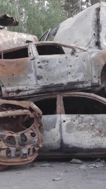 Bu stok dikey video Irpin, Bucha bölgesinde gri, düz, renksiz, yanmış arabaları gösteriyor.