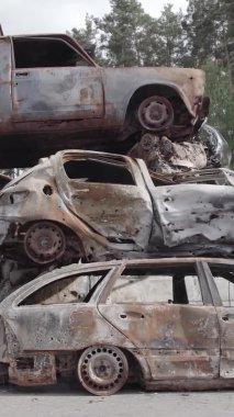 Bu stok dikey video Irpin, Bucha bölgesinde gri, düz, renksiz, yanmış arabaları gösteriyor.