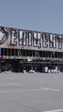 Bu dikey video, Bucha, Ukrayna 'da bir alışveriş merkezinin savaş tarafından tahrip edildiğini gösteriyor. Ağır çekim, gri, renksiz, düz.