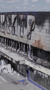 Bu dikey video, Bucha, Ukrayna 'da bir alışveriş merkezinin savaş tarafından tahrip edildiğini gösteriyor. Ağır çekim, gri, renksiz, düz.
