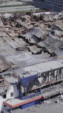 This stock vertical video shows a destroyed by war building of a shopping center in Bucha, Ukraine, slow motion, grey, no color, flat