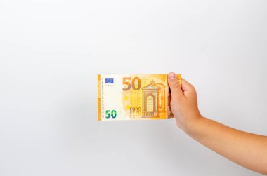 A child's hand holds a paper euro banknote on a white background. The concept of money, economy, finance, savings. Close-up