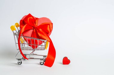 Red box with a ribbon in the form of a heart in a shopping basket on a white background. Love concept, congratulations, copy space, flat lay, banner. Close-up