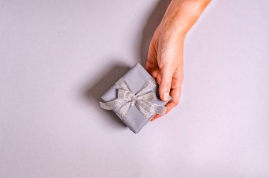 Bir kadının eli gri arka planda bir hediye kutusu tutar. Mesaj için yeri vardır. Yeni yıl ve Noel tatili kavramı, tebrikler. Uzayı kopyala Yukarıdan görüntüle