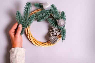 Bir kadının eli, yeni yıl çelengini gri arka planda ladin dallarıyla süslüyor. Yeni yıl ve Noel tatili kavramı, tebrikler. Yukarıdan görüntüle