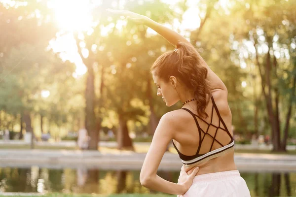Ung kvinna sträcker ut sina armar när hon idrottar i parken — Stockfoto
