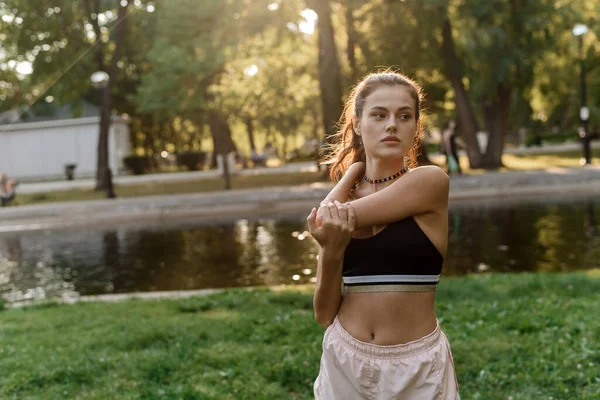 Ung kvinna sträcker ut sina armar när hon idrottar i parken — Stockfoto