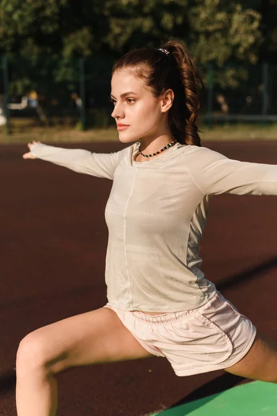 A fiatal nő kinyújtja a karját, miközben sportol a stadionban. — Stock Fotó