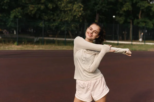 A fiatal nő kinyújtja a karját, miközben sportol a stadionban. — Stock Fotó