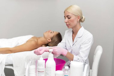 Güzel bir kadın güzellik uzmanı eldiven giyer. Müşteri kanepede yatar ve prosedürü bekler.